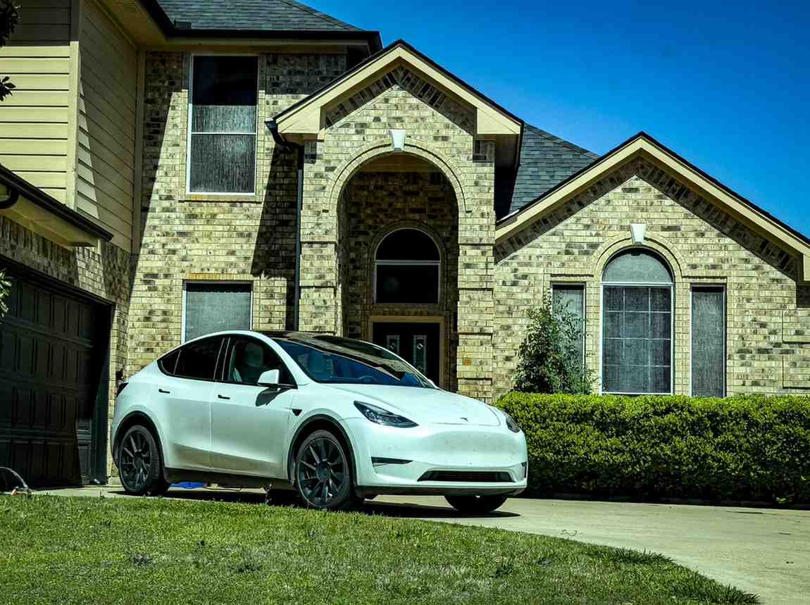 A modern electric car parked in front of a sleek house with a family smiling, representing safety and security